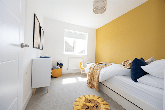 A bedroom with a bed, a yellow rug, a white wardrobe, and a window.