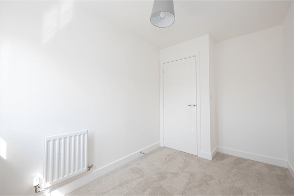 A white door is in a room with a radiator and carpet.