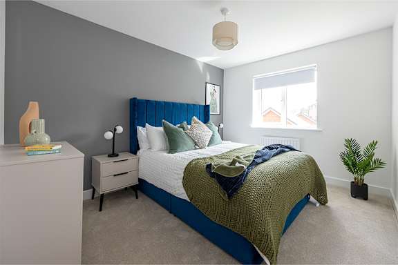 A bedroom with a bed, nightstand, and a plant.