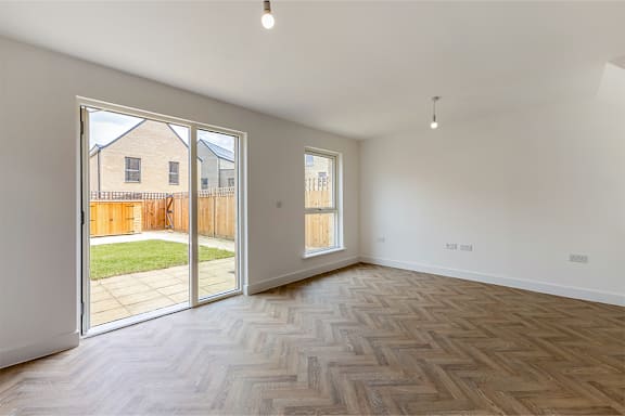A room with a wooden floor and white walls, with a view of a backyard through the glass doors.