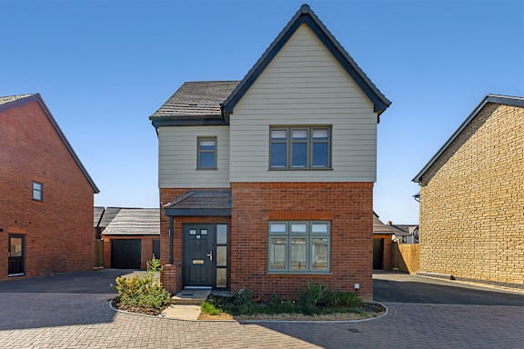 A house with a grey roof and a black door is surrounded by a brick wall.