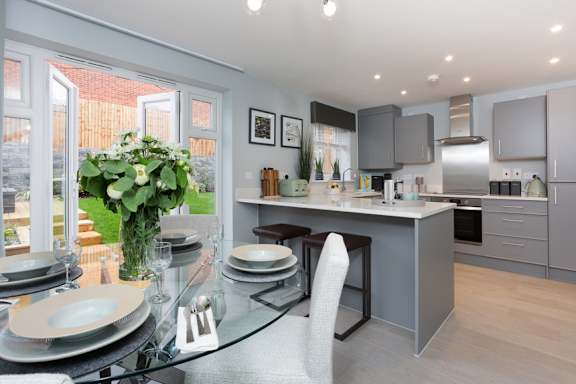 A modern kitchen with a glass dining table set for two.