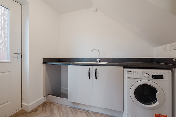 A white laundry room with a washing machine and a black countertop.