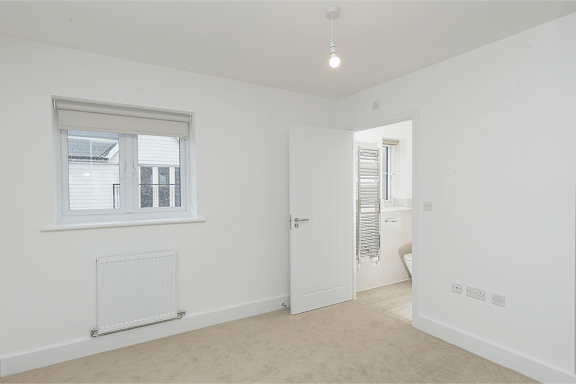 A white room with a window, a radiator, and a door leading to another room.