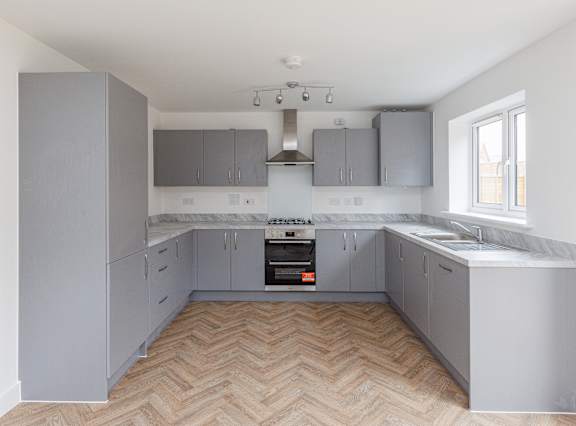 A kitchen with wooden flooring and grey cabinets.