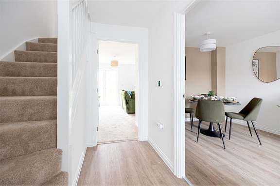 A staircase with a carpeted runner leads to a dining area with a table and chairs.