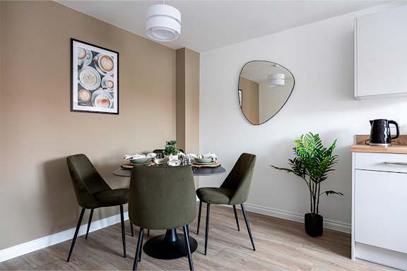 A dining room with a table set for two and a potted plant.