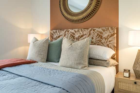 A bed with a blue comforter and a mirror above it.