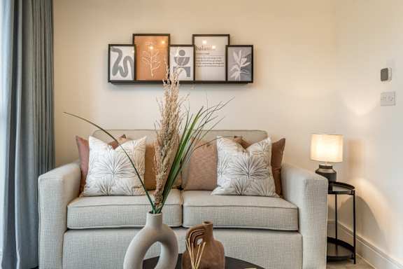 A living room with a grey couch, a vase with a plant and pictures on the wall.