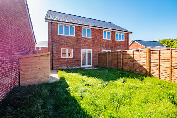 A red brick house with a wooden fence and green grass in front.