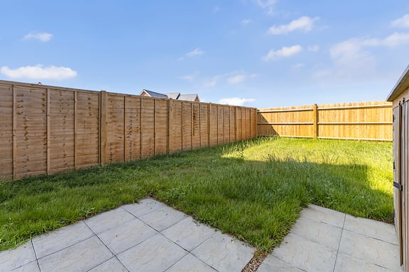 A wooden fence separates a grassy area from a paved walkway.