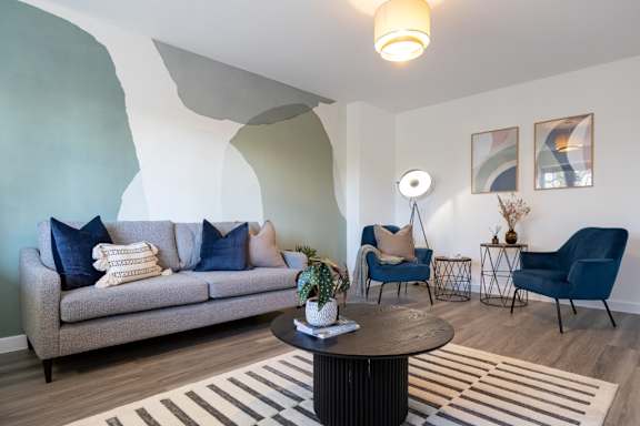 A living room with a grey couch, a blue chair, and a round table with a vase of flowers on it.