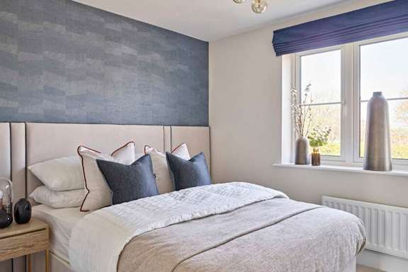A bed with a white comforter and grey pillows is in front of a window with a blue curtain.
