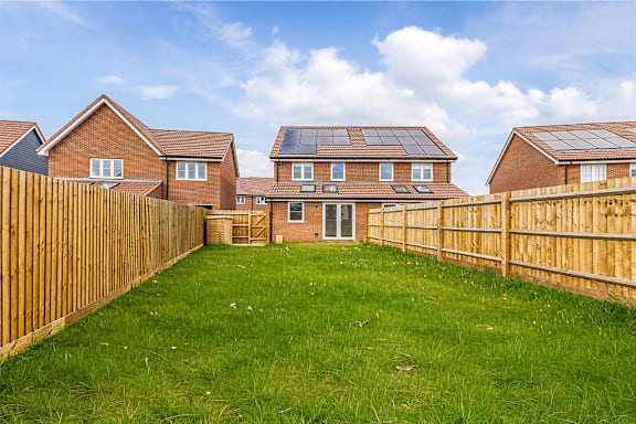 A backyard with a wooden fence and a house with solar panels on the roof.