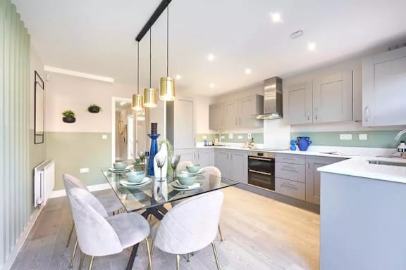 A modern kitchen with a glass dining table and white chairs.