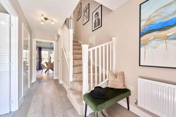 A hallway with a staircase, a green bench, and a painting on the wall.