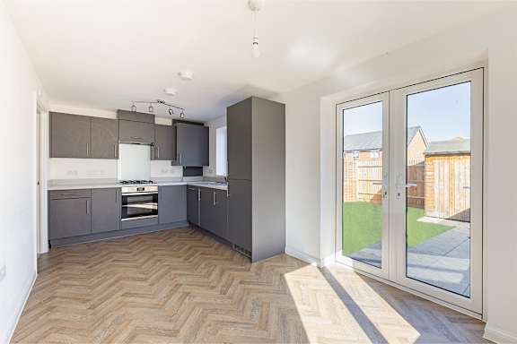 A kitchen with a wooden floor and a glass door leading to a backyard.