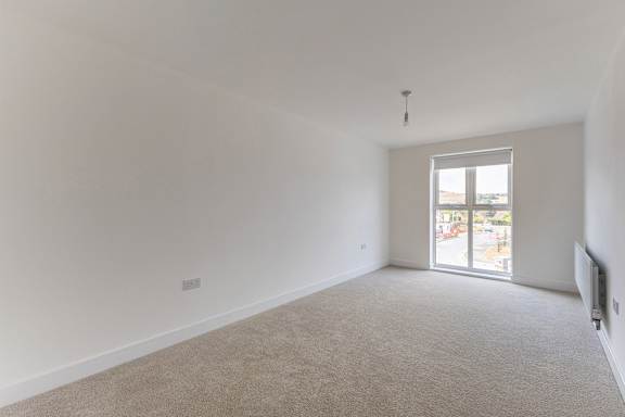 A large, empty room with a carpeted floor and a window overlooking a parking lot.