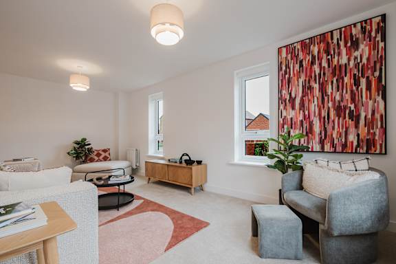 A living room with a grey couch, a red rug, a wooden table, and a large painting on the wall.