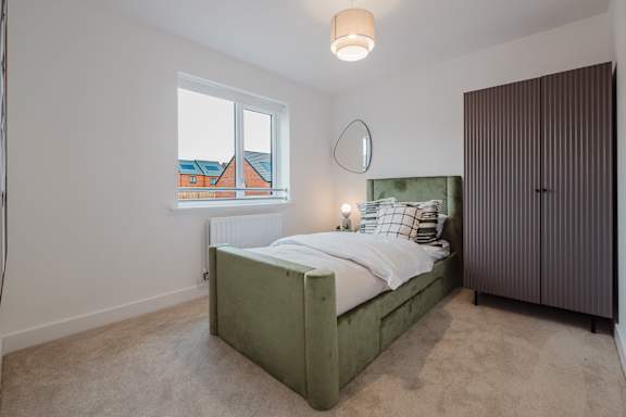 A bedroom with a green bed and a brown wardrobe.