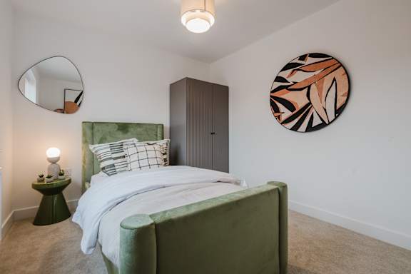 A bedroom with a green bed and a round mirror on the wall.