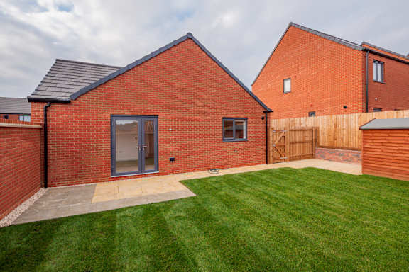 A red brick house with a grey roof and a green lawn in front.