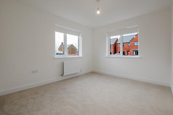 A room with a carpeted floor, two windows, and a white radiator.