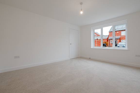 A room with a carpeted floor and a window showing a view of a red building.