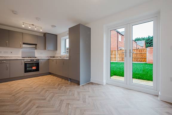 A modern kitchen with a wooden floor and a view of a backyard through the sliding glass door.