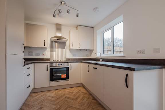 A modern kitchen with wooden flooring and white cabinets.