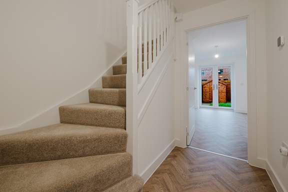 A staircase with a carpeted runner and wooden steps leads to a bright hallway.