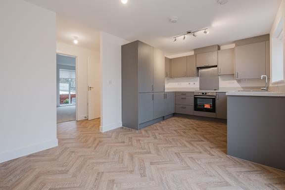 A modern kitchen with wooden flooring and grey cabinets.