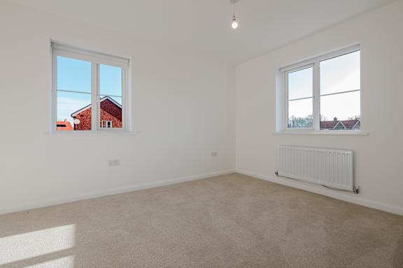 A room with a white wall and a window overlooking a red building.
