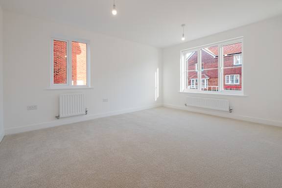 A room with white walls and carpeted floor with two windows.