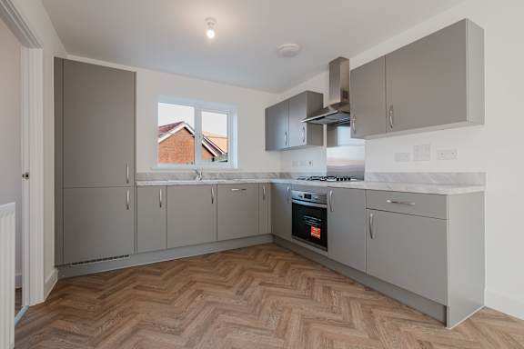 A kitchen with wooden flooring and grey cabinets.
