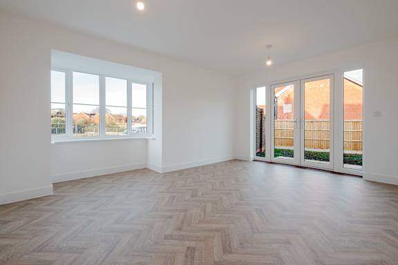 A room with a wooden floor and a view of a residential area through the windows.