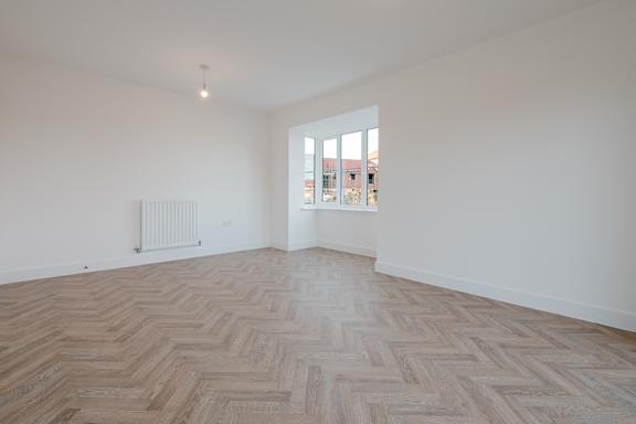 A room with a herringbone patterned floor and a window letting in light.