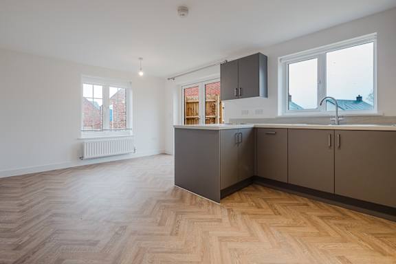 A kitchen with wooden flooring and grey cabinets.