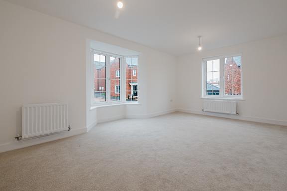A large empty room with two windows and a radiator on the wall.