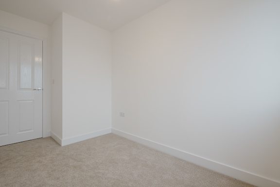 A white door is on the left side of a room with white walls and carpeted floor.