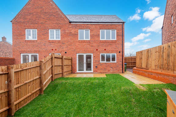 A red brick house with a wooden fence and a green lawn.