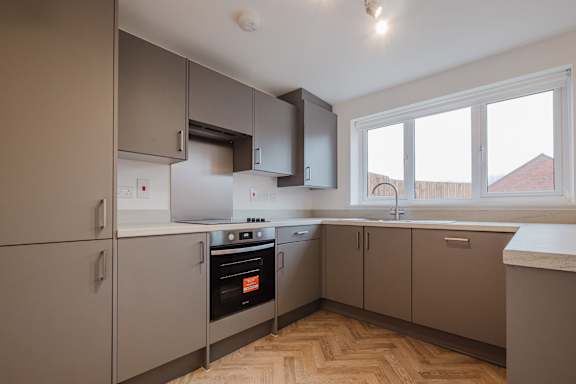 A kitchen with wooden flooring and grey cabinets.