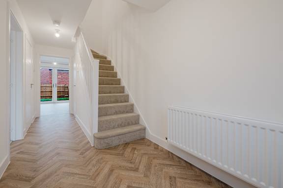 A hallway with a staircase and wooden flooring.