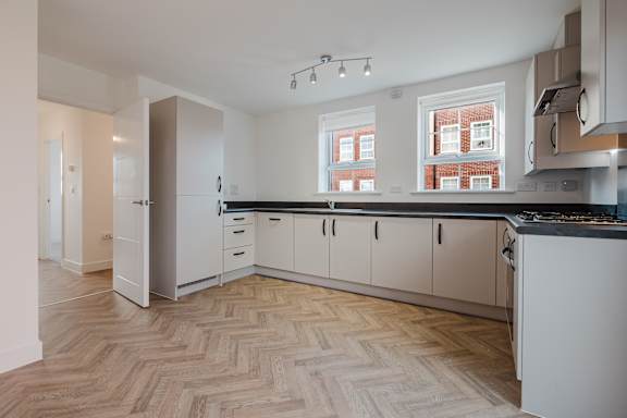 A kitchen with a white fridge, black countertops, and wooden floors.
