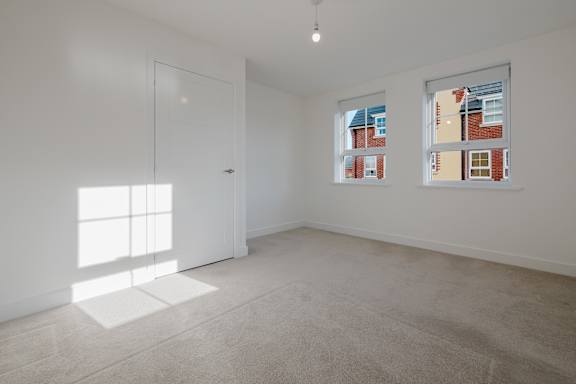 A room with a white door and windows showing a view of a building.