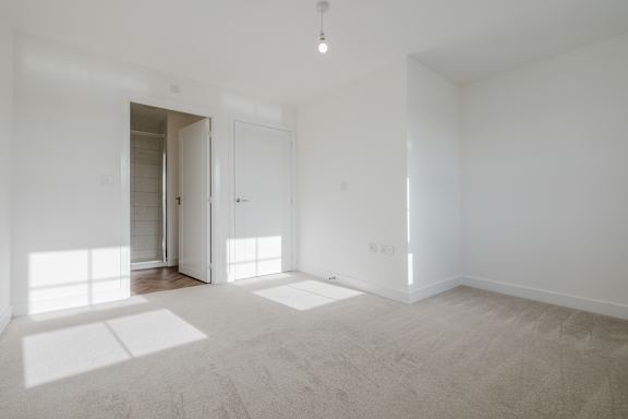 A white room with a carpet floor and a doorway leading to another room.