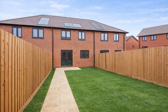 A long wooden fence separates a green lawn from a brick building.