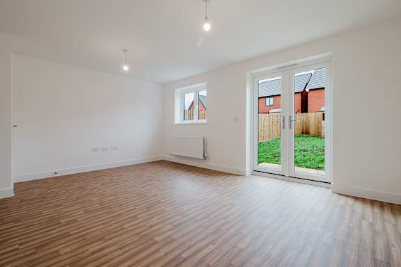 A room with wooden flooring and a window overlooking a backyard.