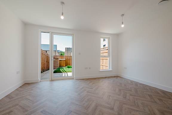 A room with a wooden floor and white walls, with a view of a backyard through a sliding glass door.