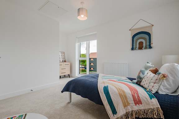 A bedroom with a bed, a nightstand, a window, and a wall hanging.